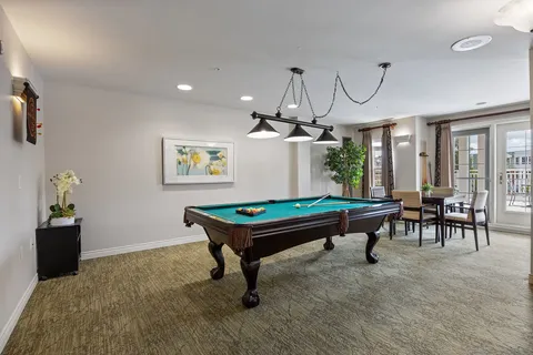 Billiards table beneath hanging lights beside large windows