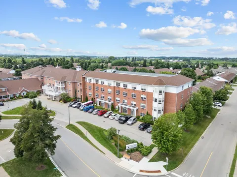 Aerial view of a brick residence building beside a driveway and parked cars