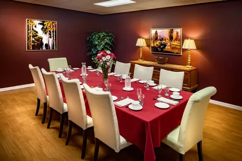 Dining room with a long table, white chairs and red tablecloth
