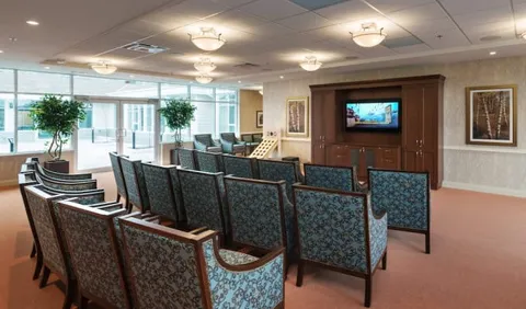Rows of patterned chairs facing a television in a room with large windows
