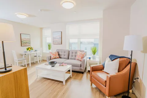 Room with a grey sofa, brown armchair, white coffee table and small dining table