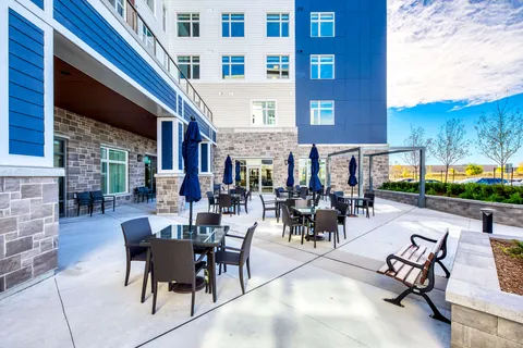 Patio with tables, chairs, closed umbrellas and benches beside the building