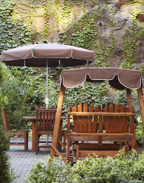 Wooden garden swing and patio furniture beside an ivy-covered wall