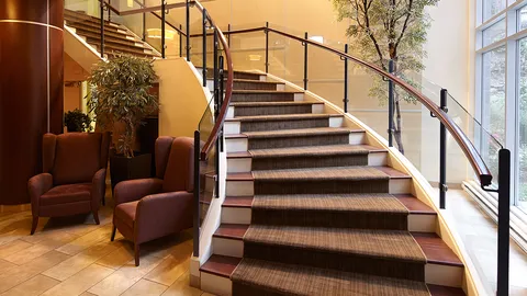 Curving staircase with metal railings, armchairs and tall windows