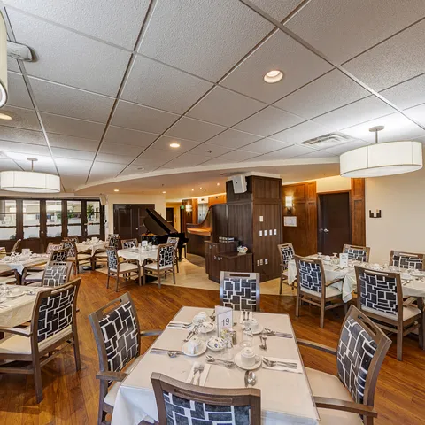 Dining room with set tables, patterned chairs, hanging lights and a grand piano