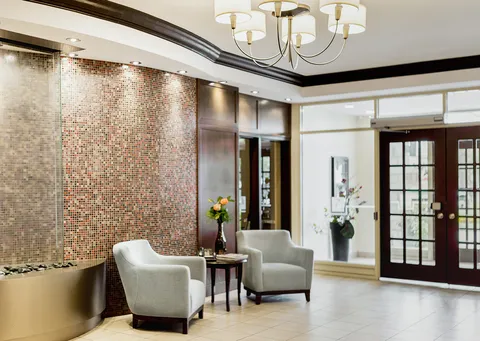 Armchairs and a small table beside glass doors and a curved mosaic wall