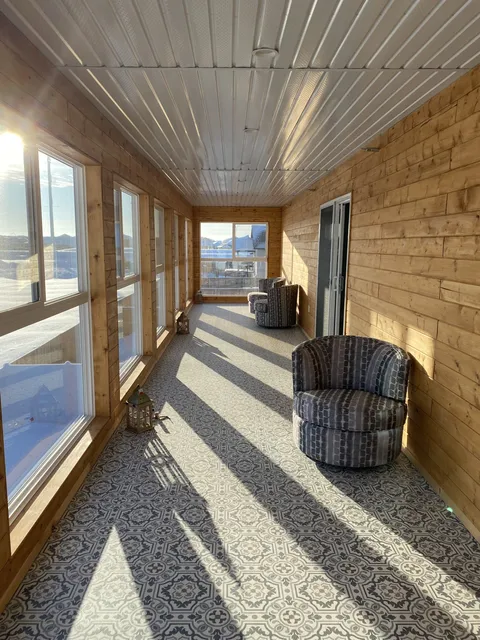 Covered porch with chairs, windows and a wooden railing.