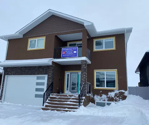 Front of the two-storey residence with steps, a garage and snow.