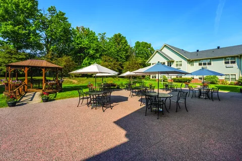 Patio tables and chairs beneath umbrellas beside a garden