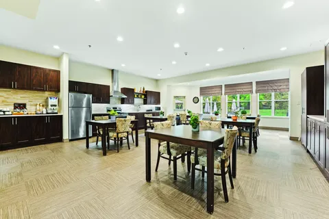 Tables and chairs beside a kitchenette with wooden cabinets