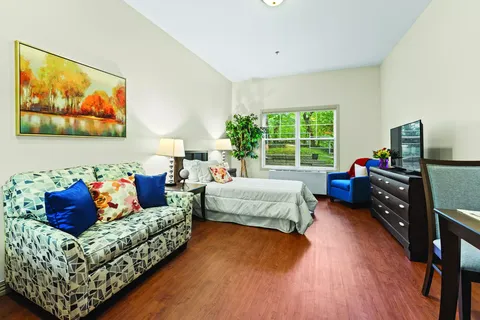 Sitting area with a sofa, television and a bed beside large windows