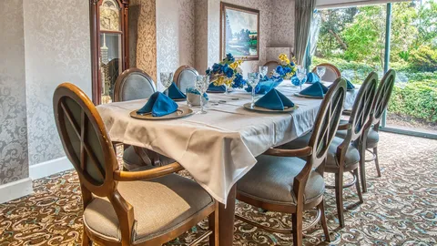 Dining table beside a window with blue napkins and a grandfather clock