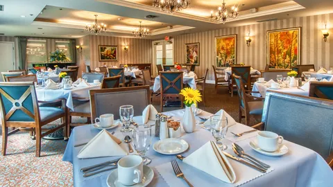 Dining room with white tablecloths, blue chairs, chandeliers and floral paintings