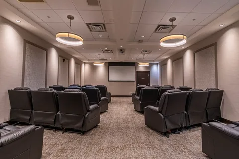 Cinema room with rows of black reclining chairs and a blank projection screen