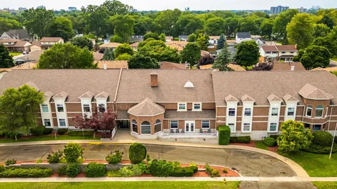Aerial view of a brick residence with a curved driveway and surrounding trees