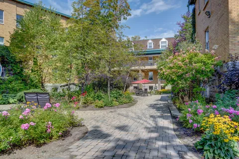 Paved courtyard path beside flowering plants, brick walls and patio furniture