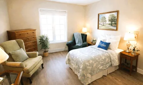 Furnished bedroom with a bed, armchairs and wooden dresser.