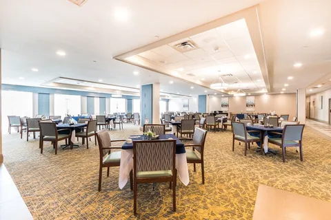 Dining room with set tables, upholstered chairs and large windows.