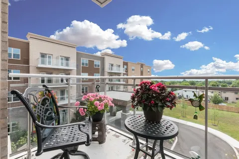 Balcony with a table, metal chairs and flower planters.