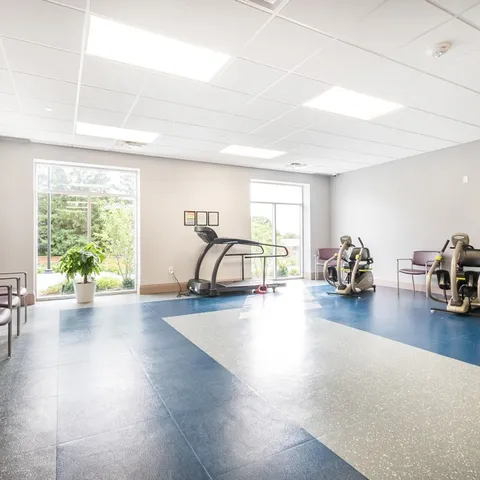 Fitness room with exercise machines and windows.