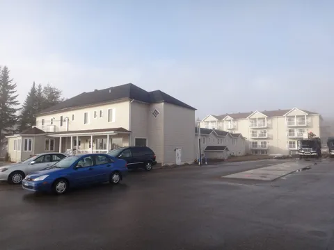 Cream residential buildings beside a paved driveway and parked cars