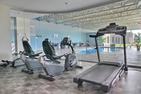 Exercise machines beside a glass wall overlooking an indoor pool