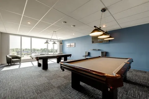 Two billiards tables beside large windows and a blue wall