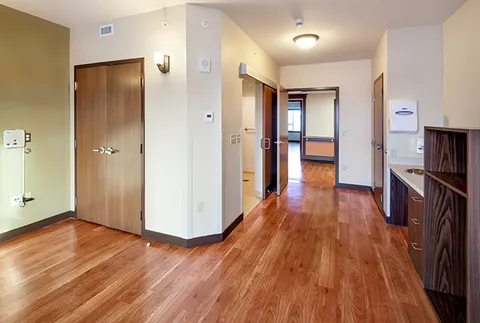 Empty room with wood flooring, a closet, kitchenette and bathroom doorway