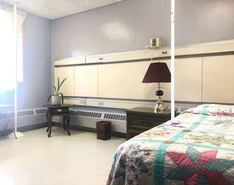 Bedroom with a patchwork quilt, dark bedside table, lamp and potted plant