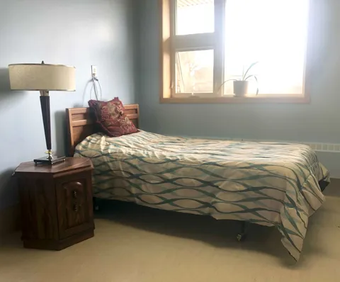 Bedroom with a striped bedspread, wooden headboard and lamp beside a window