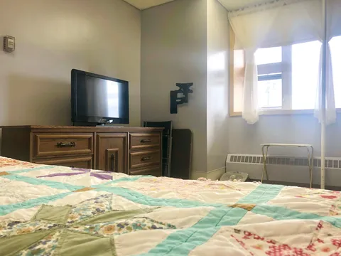 Bedroom with a patchwork quilt, wooden drawers, television and curtained window
