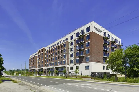 Multi-storey residence with balconies beside a roadway and landscaping.