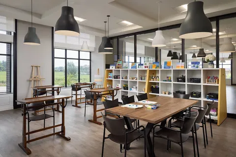 Activity room with tables, chairs, shelves and large windows.