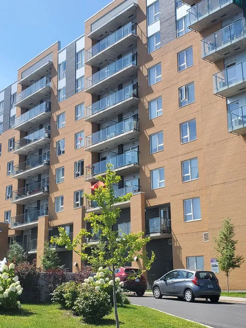 Multi-storey building with brick walls and glass-railed balconies beside a lawn