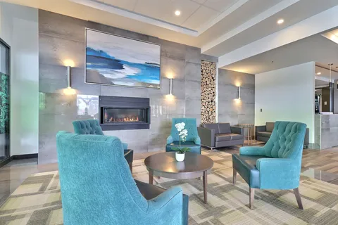 Room with turquoise armchairs, tables and a fireplace beneath a seascape