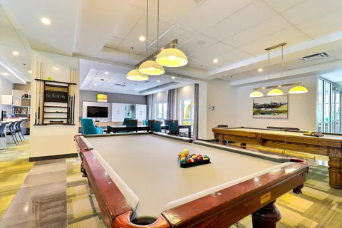 Room with two pool tables, pendant lights and upholstered seating