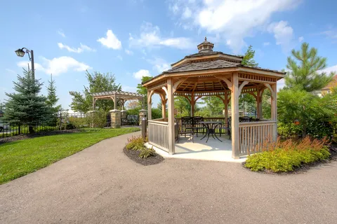 Wooden gazebo surrounded by a paved path, lawn and flower beds