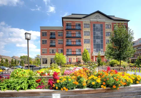 Brick residence building behind colourful flower beds and trees