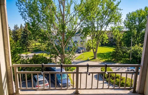 Balcony overlooking trees, a lawn, a street and parked cars