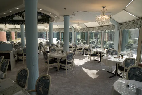 Dining room with round tables, blue patterned chairs and chandeliers