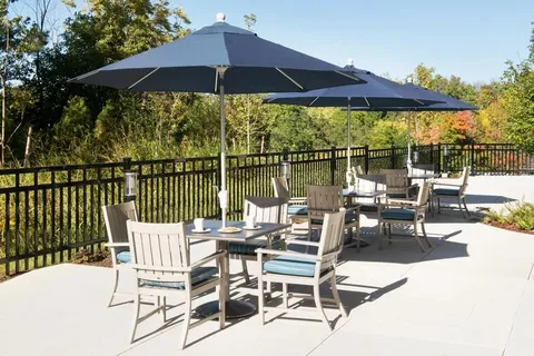 Patio tables and chairs under dark umbrellas beside a black railing