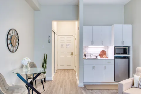 Suite dining area beside a white kitchenette and hallway.