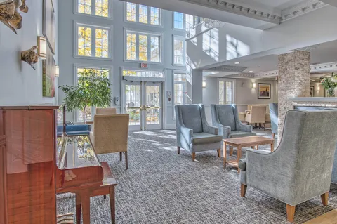 Lounge with armchairs beside tall windows and a stone fireplace.