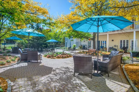 Garden courtyard with patio chairs, blue umbrellas and trees.