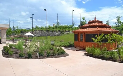 Wooden gazebo beside a paved garden path and planted beds