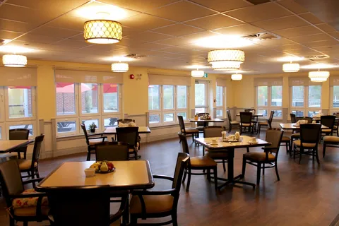 Dining room with small tables, upholstered chairs and windows along two walls.