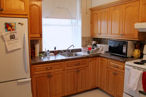 Apartment kitchen with wood cabinets, a sink, stove, microwave and refrigerator.