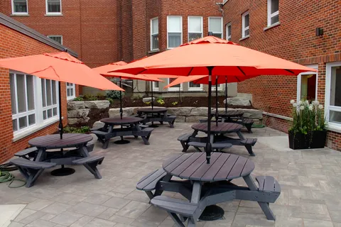 Paved courtyard with picnic tables and red umbrellas beside the brick building.