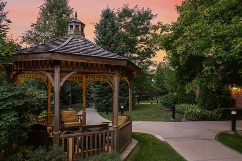 Wooden gazebo beside trees and a paved garden path.
