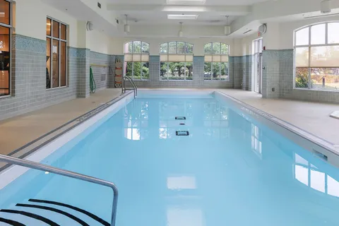 Indoor swimming pool with handrails and tall windows.